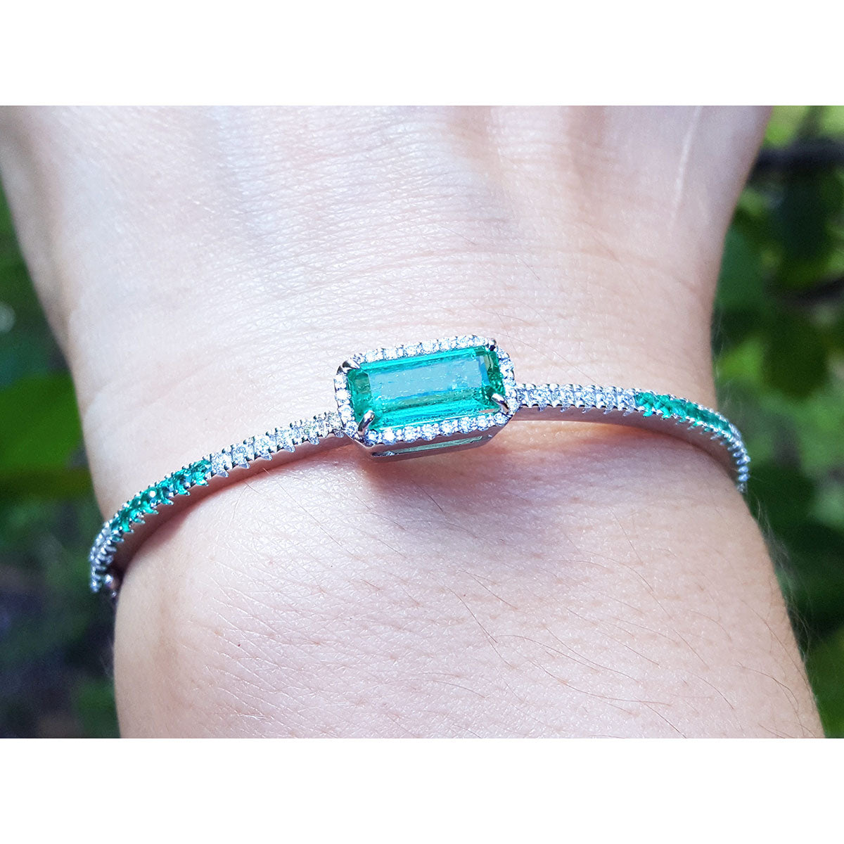 Close-up of a bangle bracelet with a natural emerald gemstone on a wrist against a blurred natural background