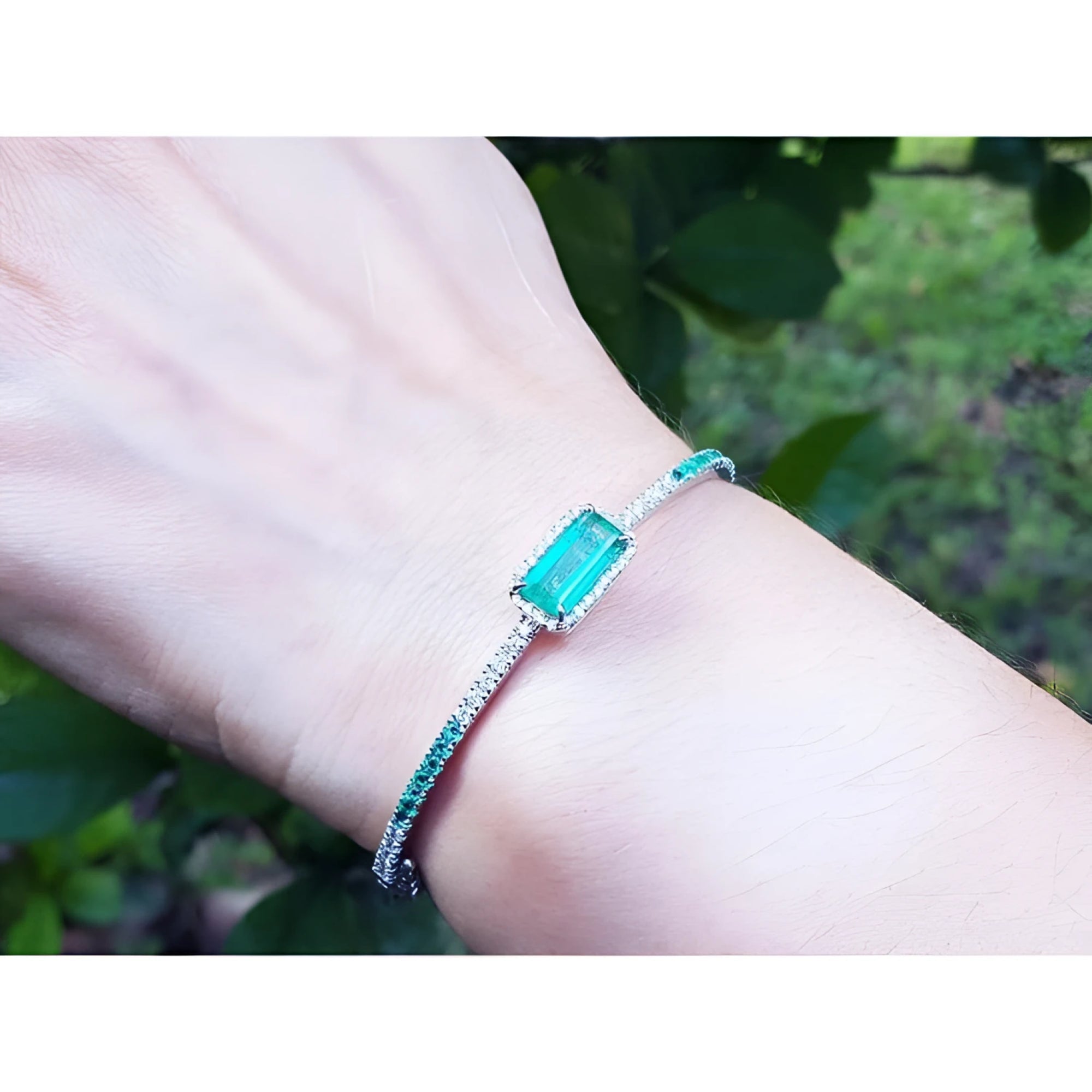 Emerald-cut Colombian emerald bangle bracelet with natural diamonds in 14K white gold on a wrist.