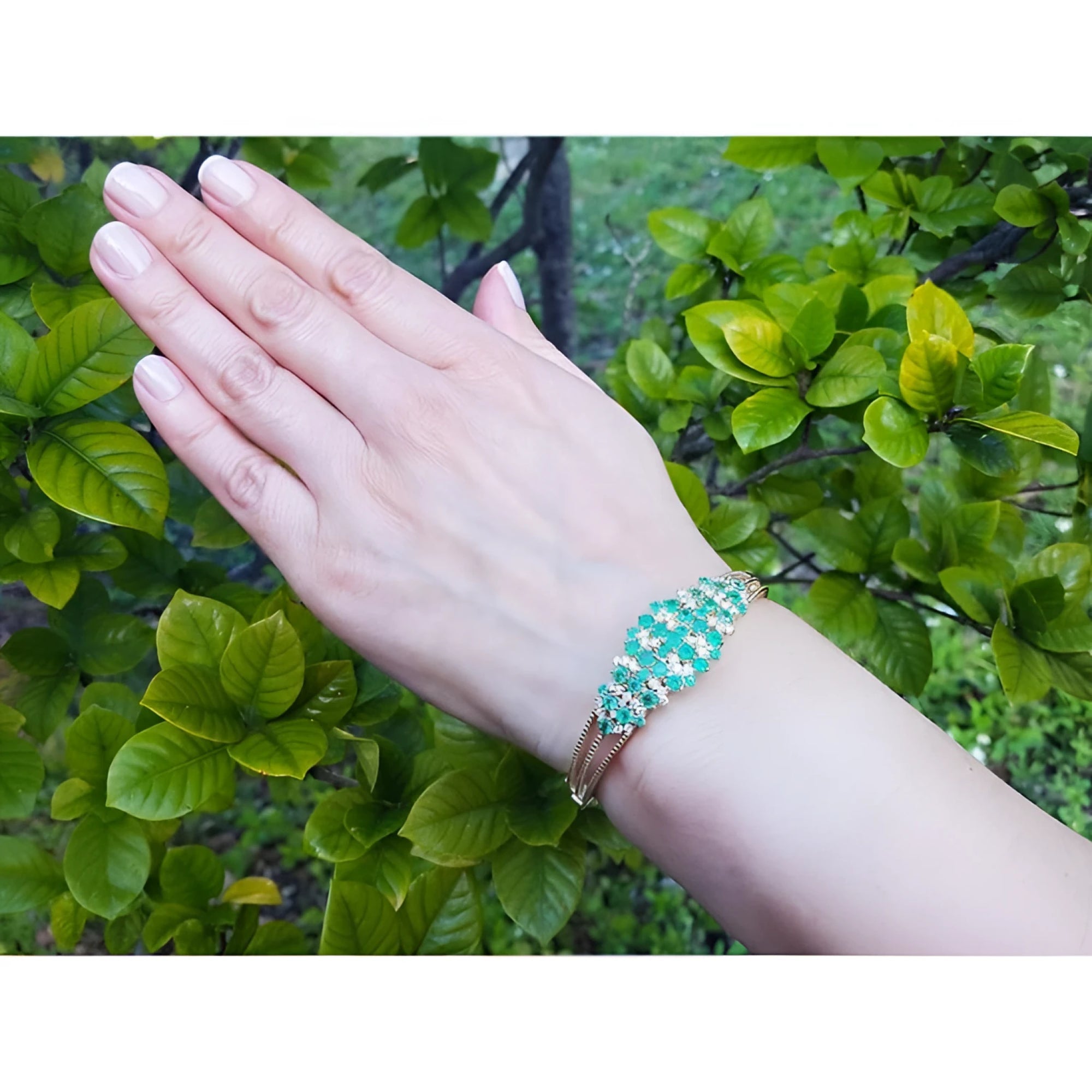 14K yellow gold bangle with round Colombian emeralds and diamonds in a floral design on a hand.