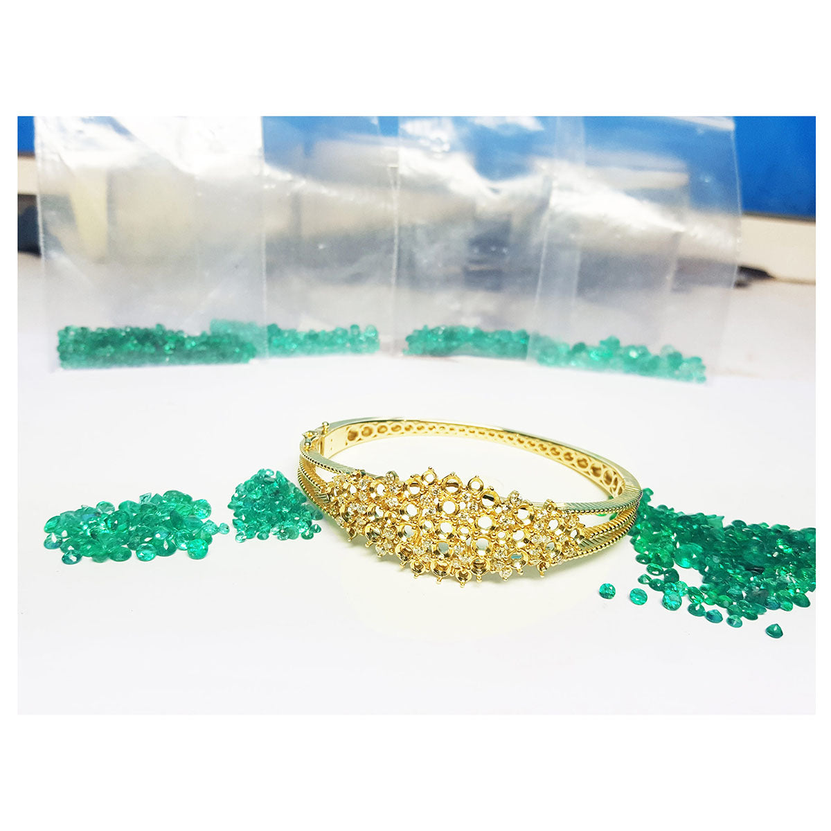 Gold bracelet with natural loose emeralds on a white surface.