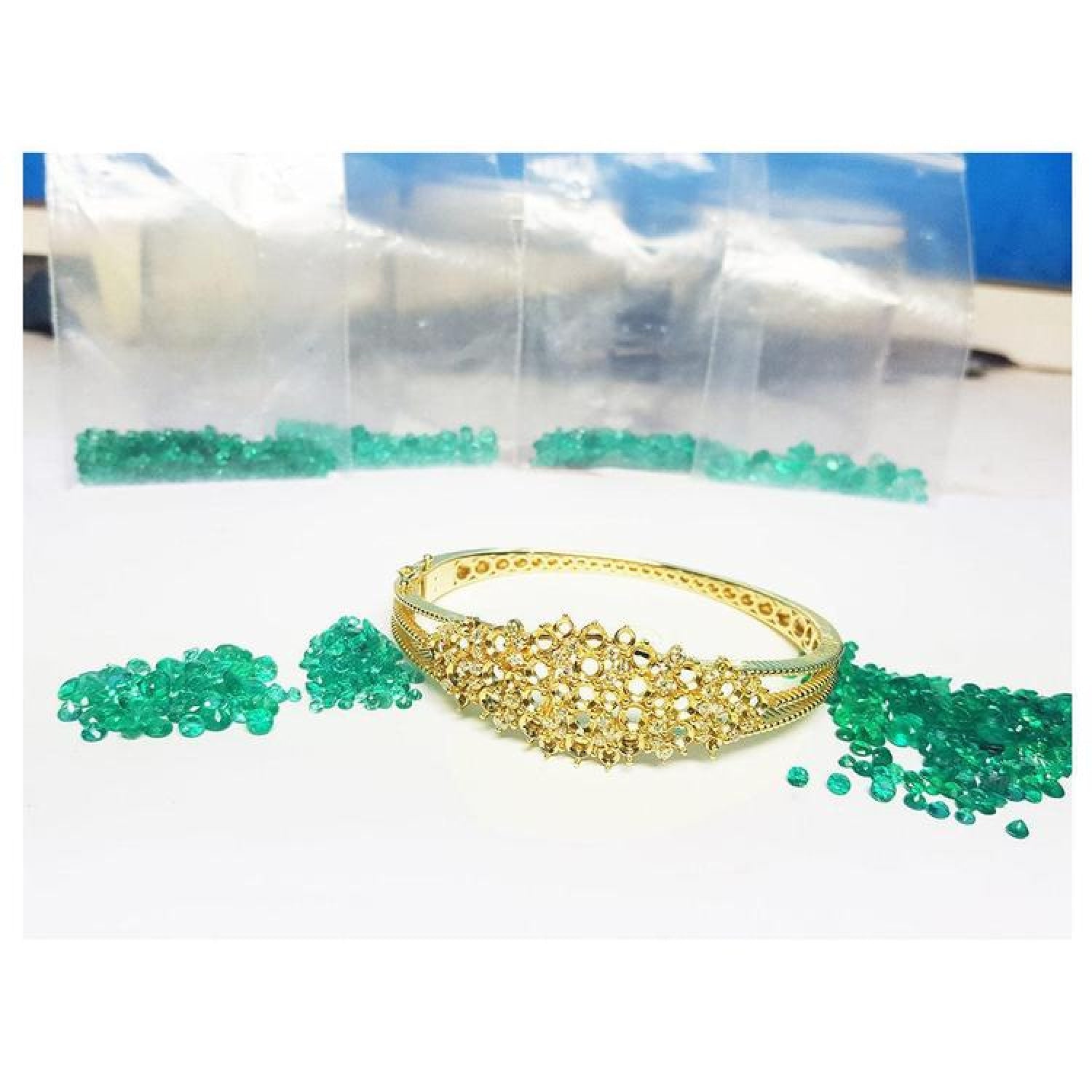 14K yellow gold bangle with round Colombian emeralds and diamonds in a floral design.