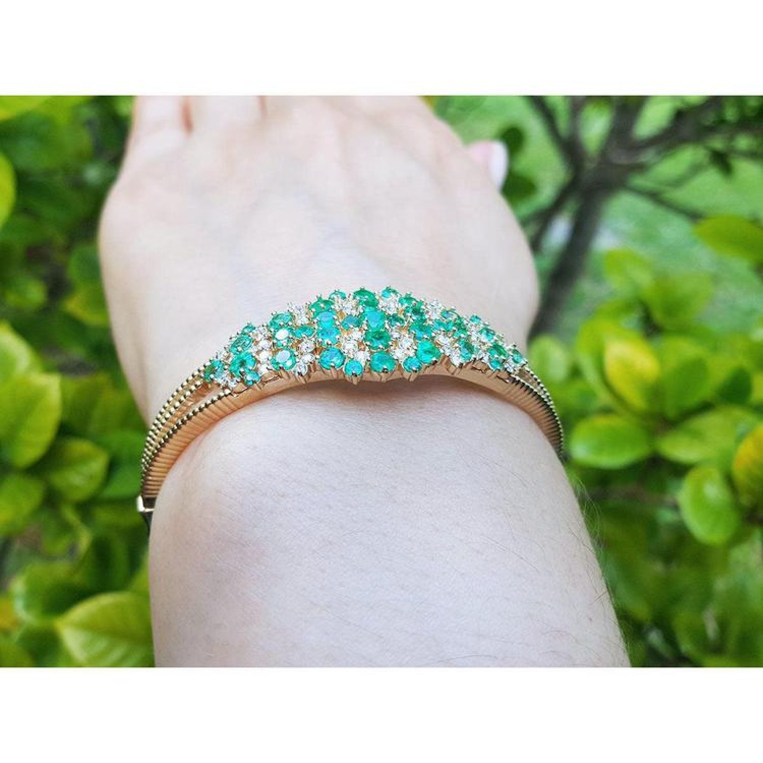 14K yellow gold bangle with round Colombian emeralds and diamonds in a floral design.