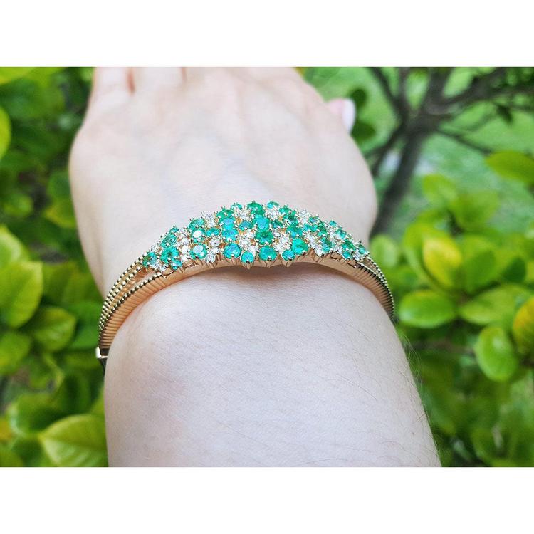 14K yellow gold bangle with round Colombian emeralds and diamonds in a floral design.
