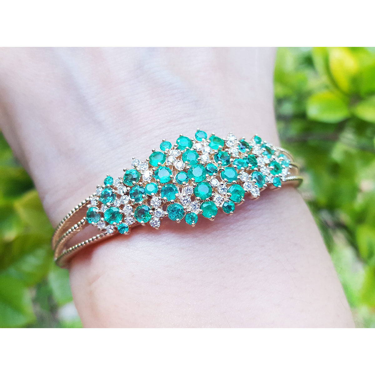 An emerald bangle bracelet round cut Colombian emeralds and natural diamonds in 14k yellow gold on a wrist.