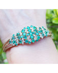 An emerald bangle bracelet round cut Colombian emeralds and natural diamonds in 14k yellow gold on a wrist.