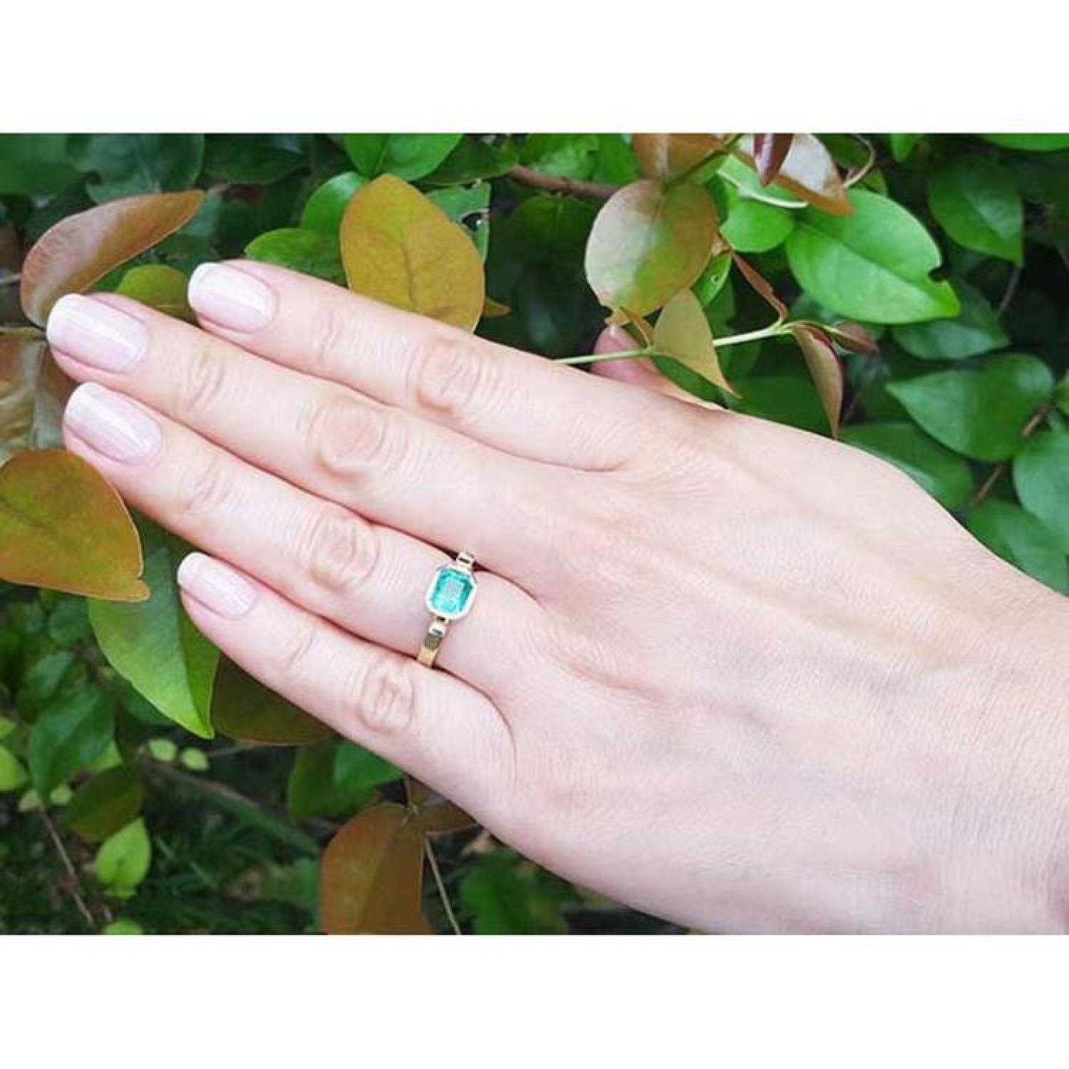 0.93 ct. solitaire emerald cut Colombian emerald ring in 14K yellow gold on a hand.