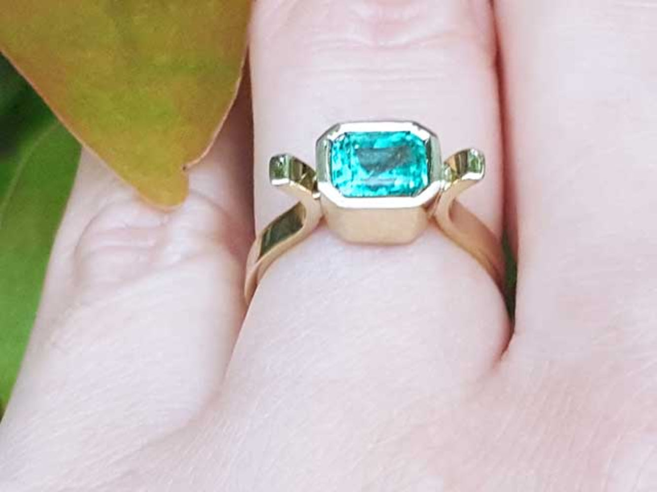 A yellow gold emerald ring held between fingers