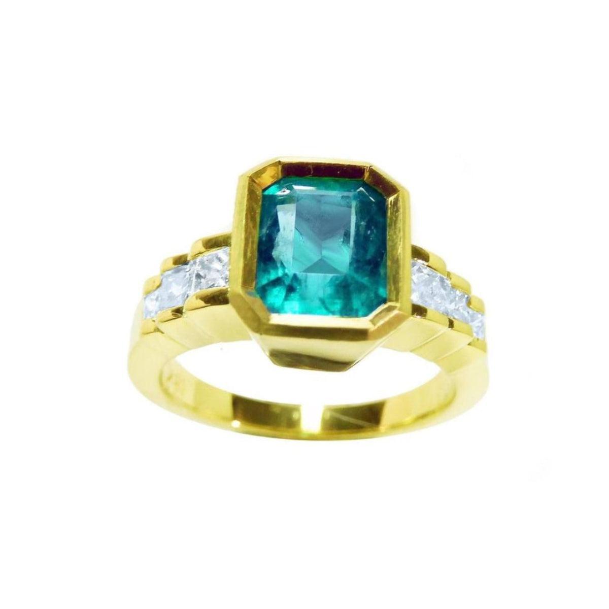 A women's bezel set emerald ring with accent princess cut diamonds on a top profile view position.