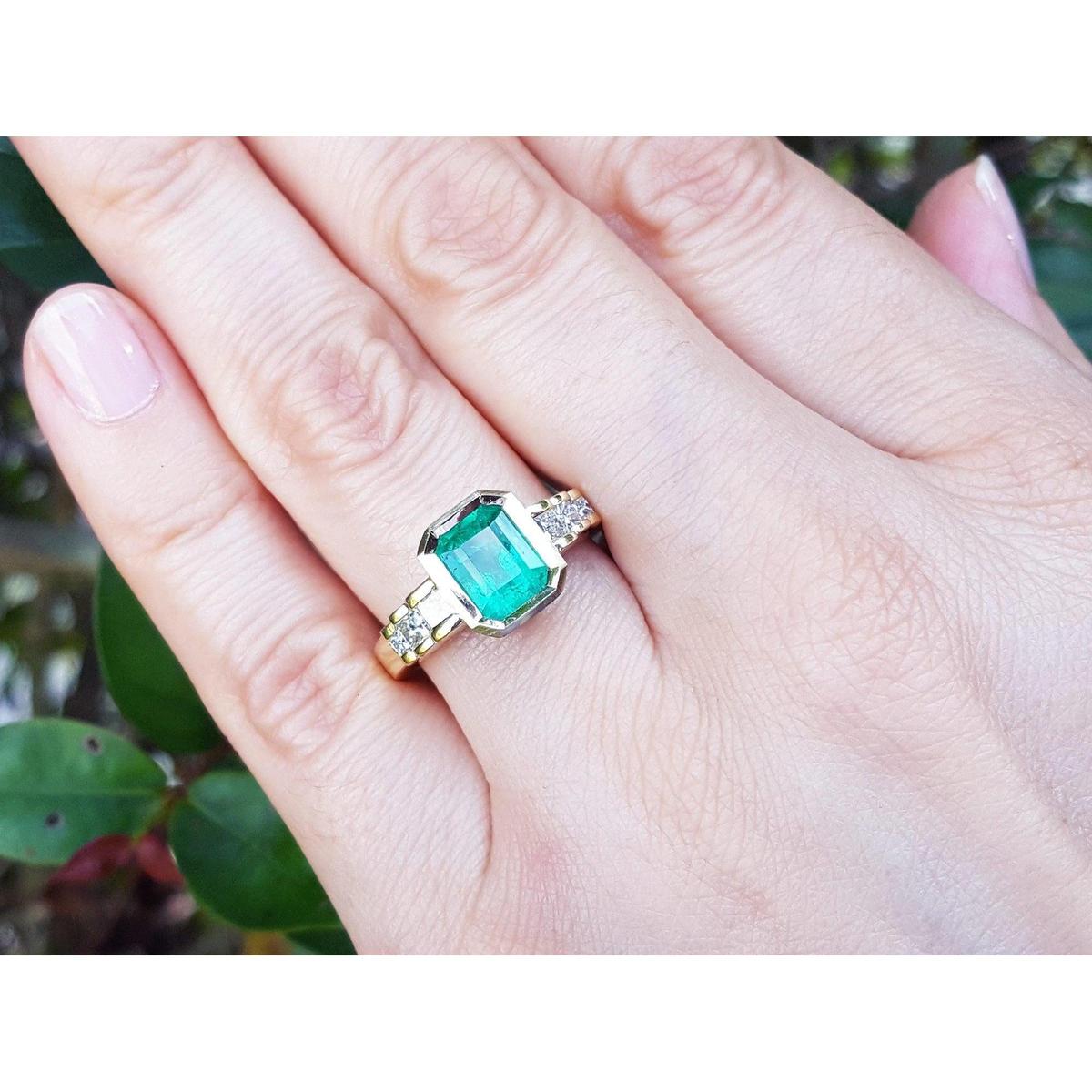 A May's birthstone brides' emerald engagement ring on a hand against a blurred natural background.