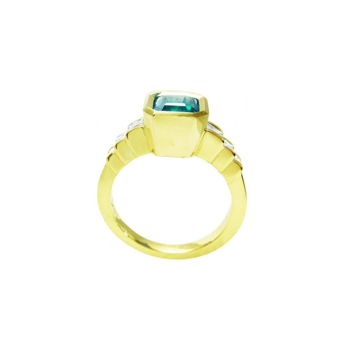 This bezel set emerald ring with accent princess cut diamonds is displaying its high top and lateral gallery.