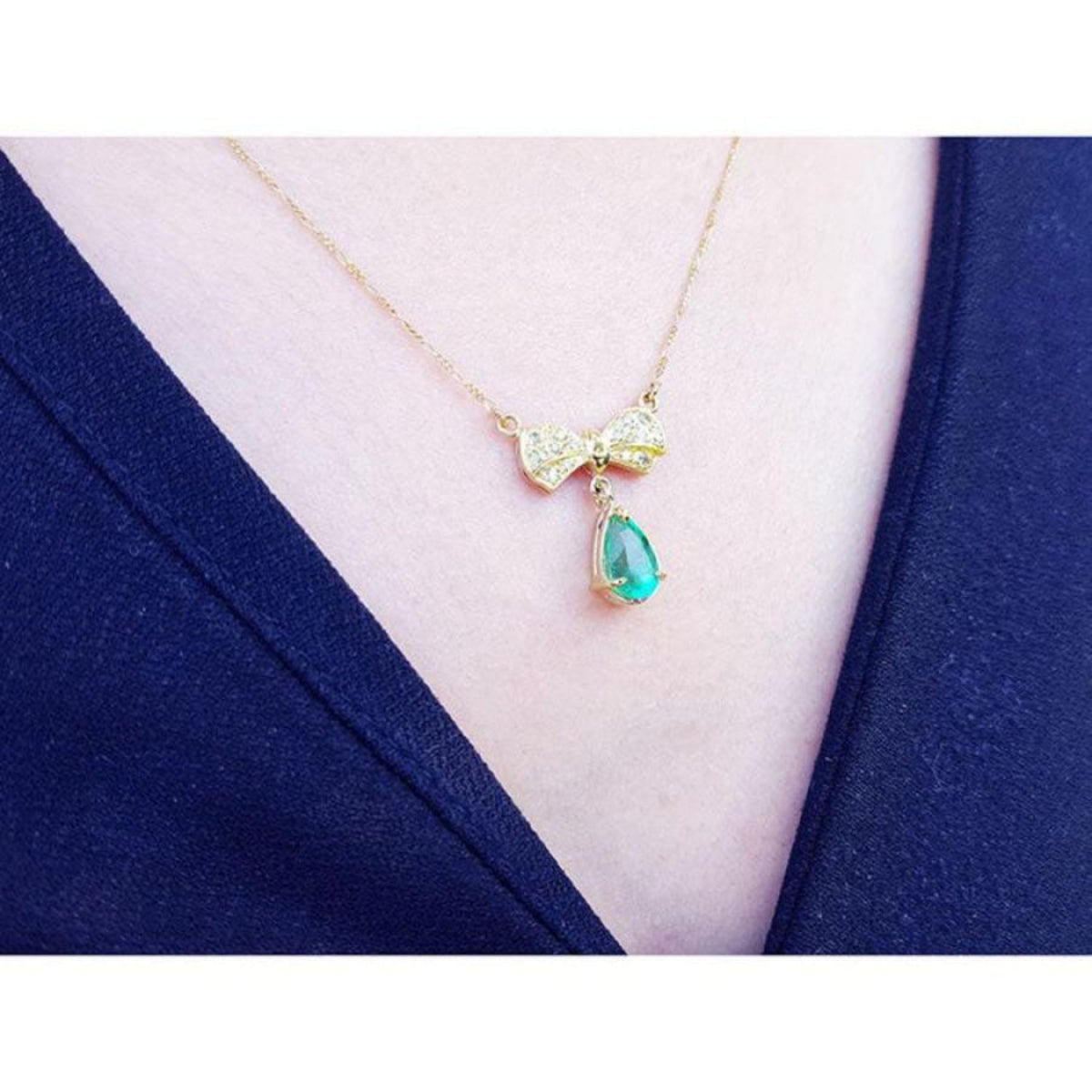 18K yellow gold bow-tie necklace with pave diamonds and a dangling pear-shaped emerald.