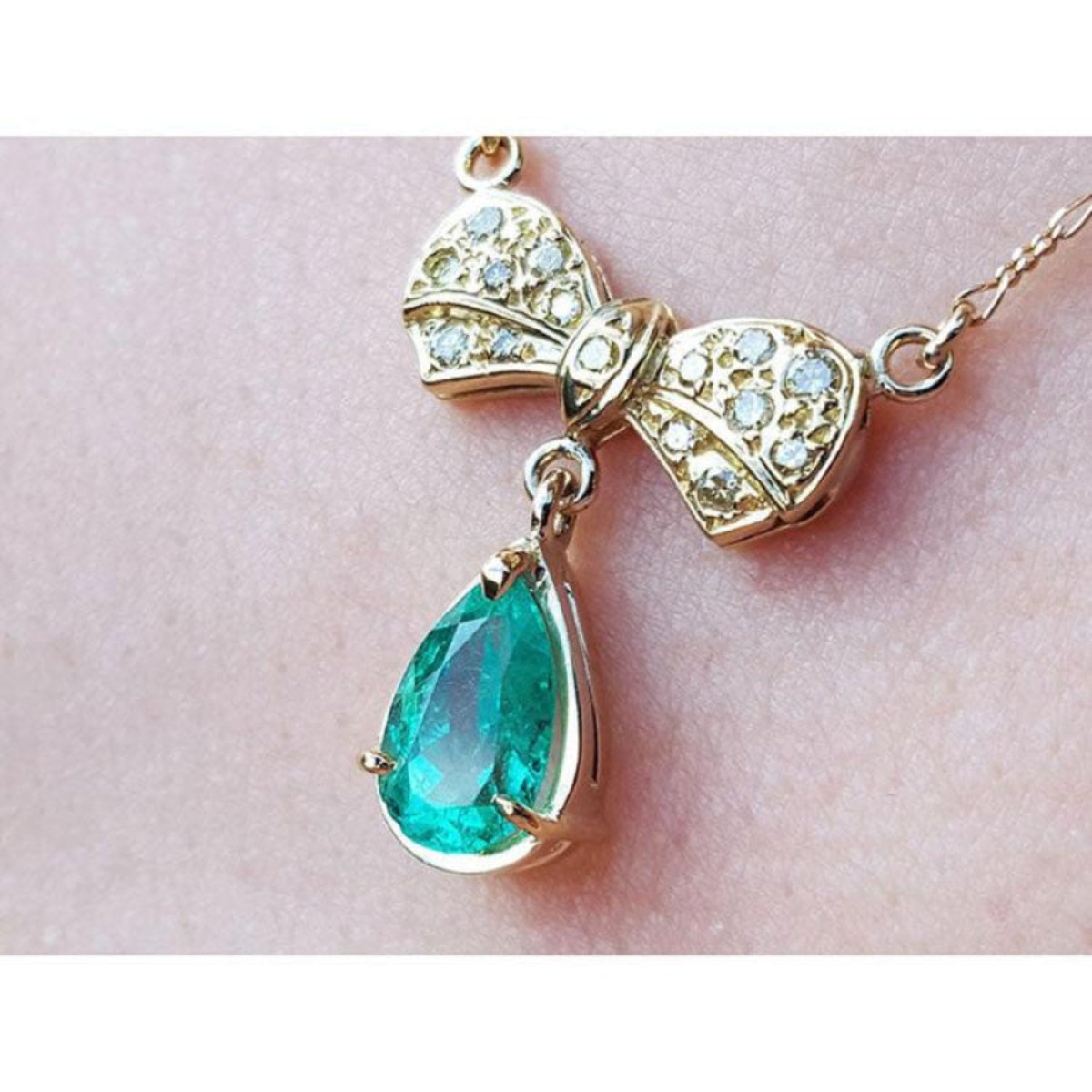 18K yellow gold bow-tie necklace with pave diamonds and a dangling pear-shaped Colombian emerald.