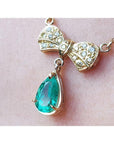 18K yellow gold bow-tie necklace with pave diamonds and a dangling pear-shaped Colombian emerald.