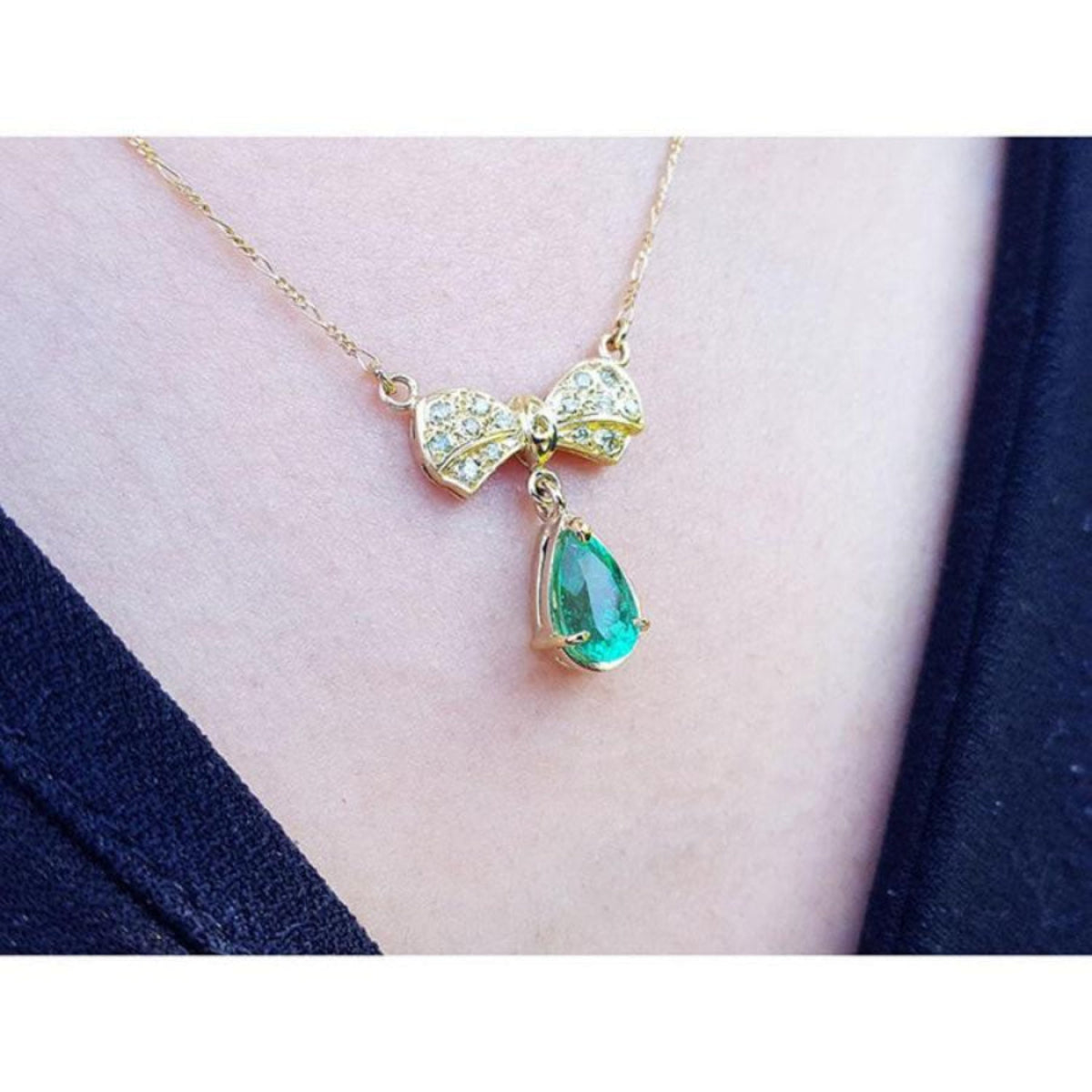 18K yellow gold bow-tie necklace with pave diamonds and a dangling pear-shaped emerald.