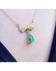 18K yellow gold bow-tie necklace with pave diamonds and a dangling pear-shaped emerald.
