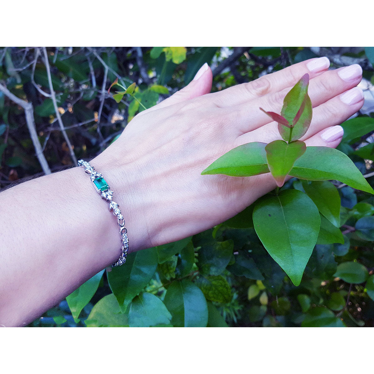 Hand wearing a bracelet with a genuine emerald against a natural background.