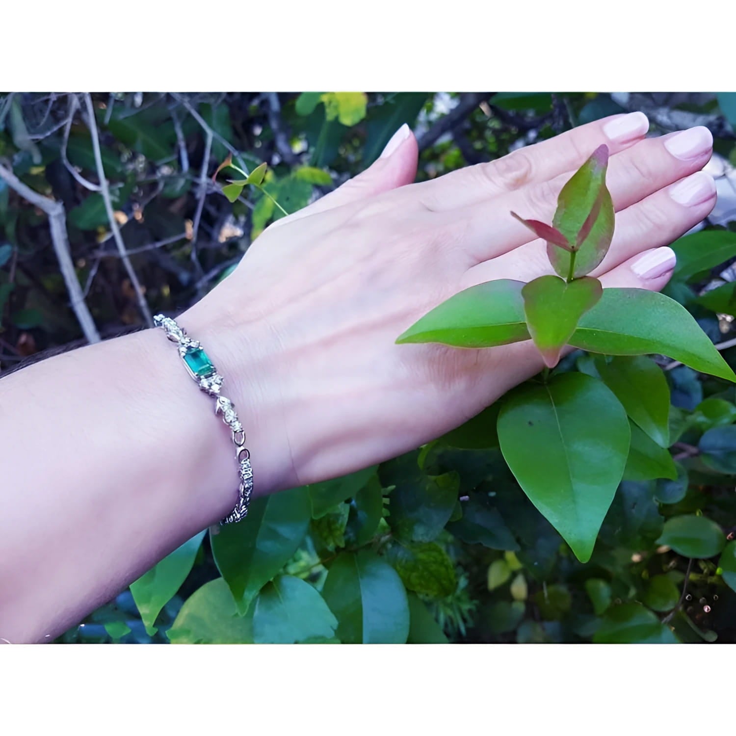 14K white gold bracelet with a rectangular Muzo Colombian emerald and six diamond accents on a woman's wrist.