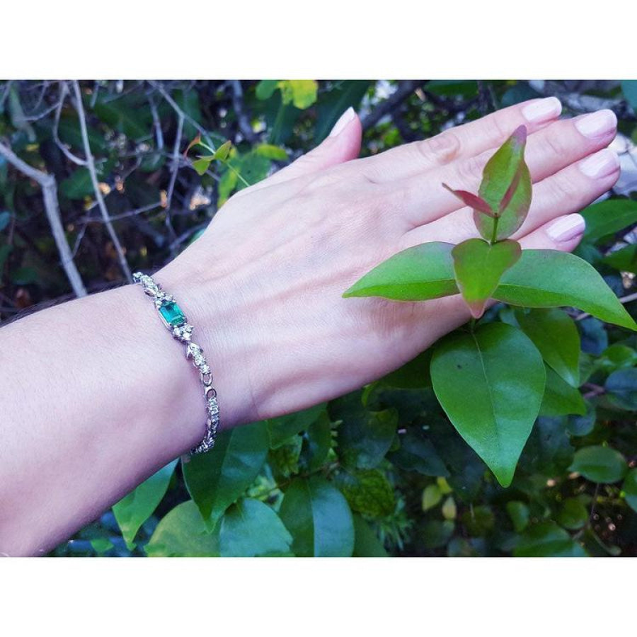 14K white gold bracelet with a rectangular Muzo Colombian emerald and six diamond accents on a woman's wrist.
