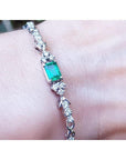 An emerald-cut Muzo Colombian emerald bracelet natural diamonds 14k white gold on a wrist.
