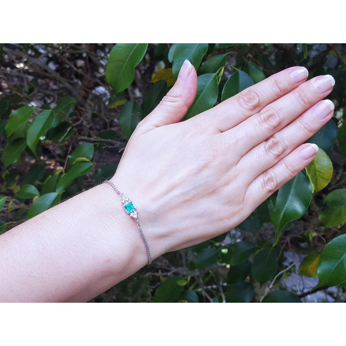 Woman&#39;s and wearing a bracelet with a natural emerald against a leafy background.
