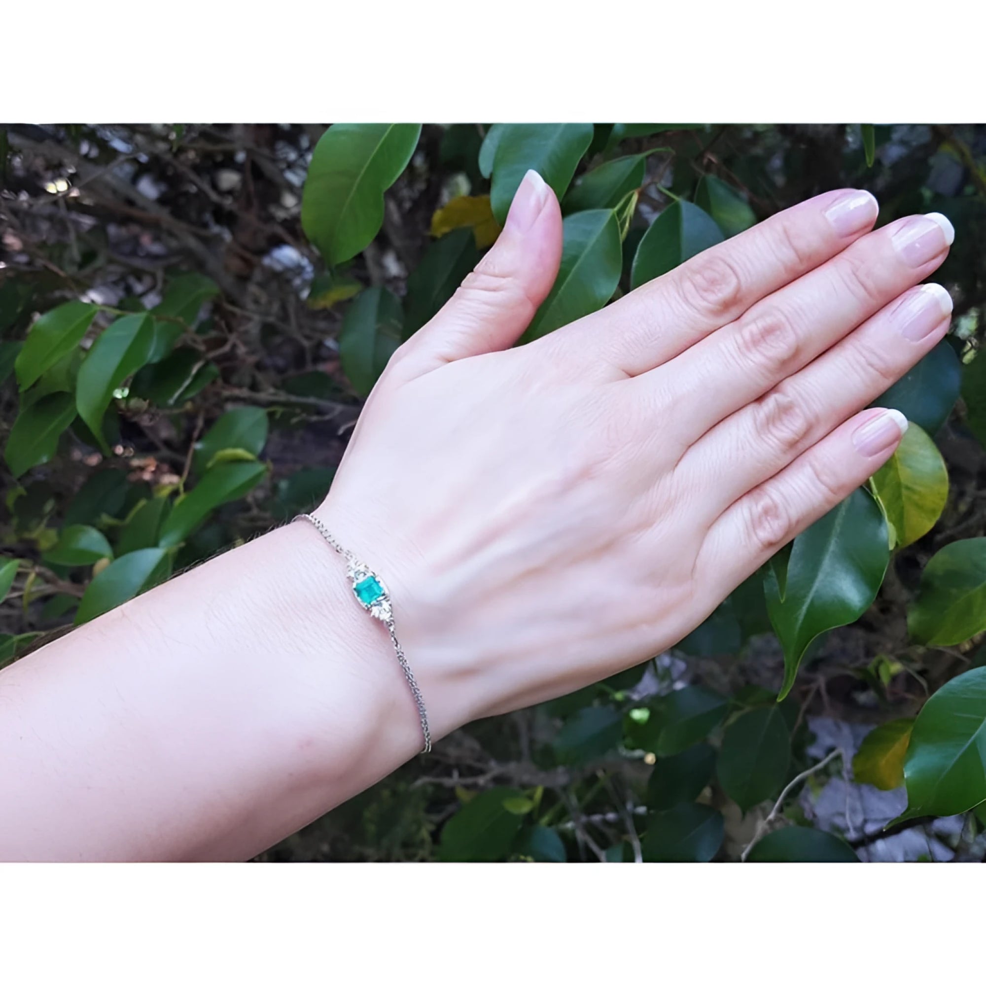 14K white gold bracelet with a sparkling emerald-cut Colombian emerald and diamonds on a woman's wrist.