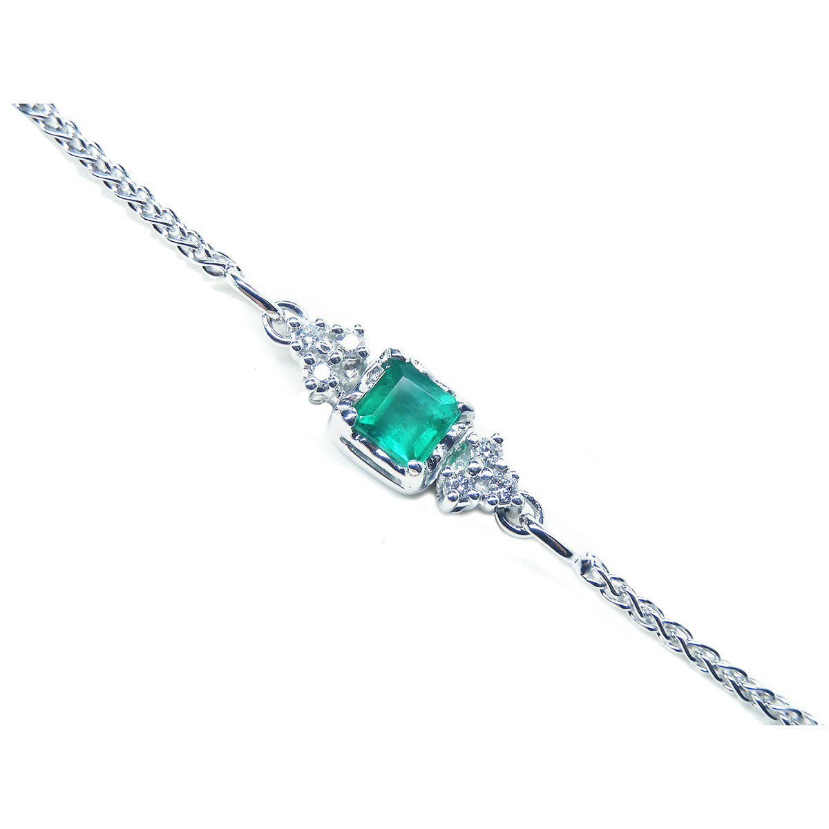 A close-up of a white gold bracelet with a natural emerald and diamonds on a white background.