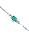 A close-up of a white gold bracelet with a natural emerald and diamonds on a white background.