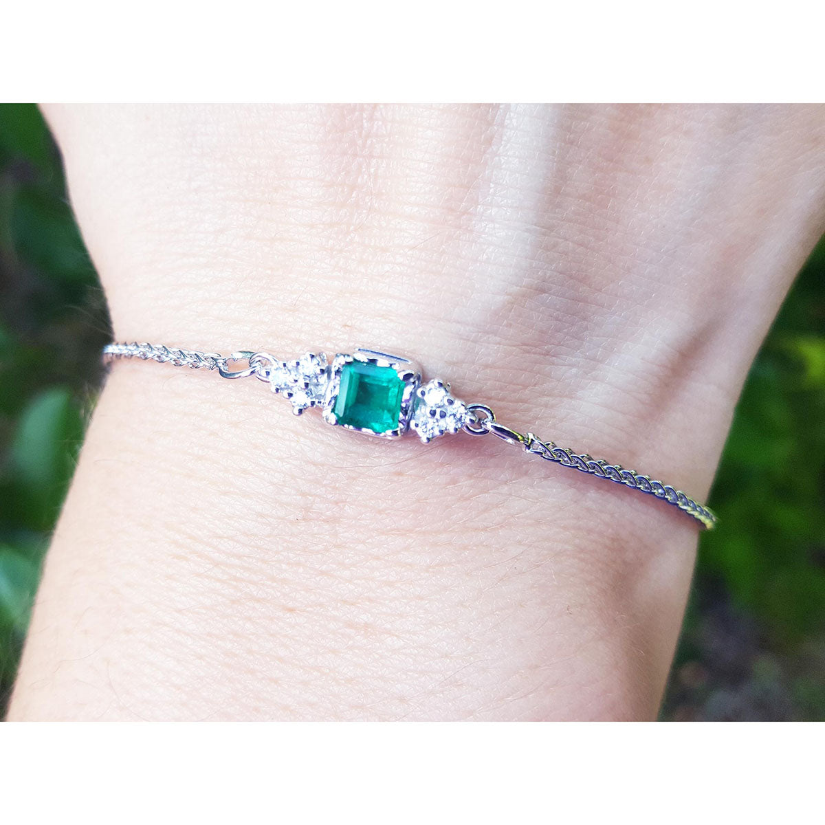 A square emerald-cut bracelet Colombian emerald and diamond in white gold on a wrist against a blurred natural background.