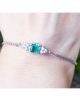 A square emerald-cut bracelet Colombian emerald and diamond in white gold on a wrist against a blurred natural background.