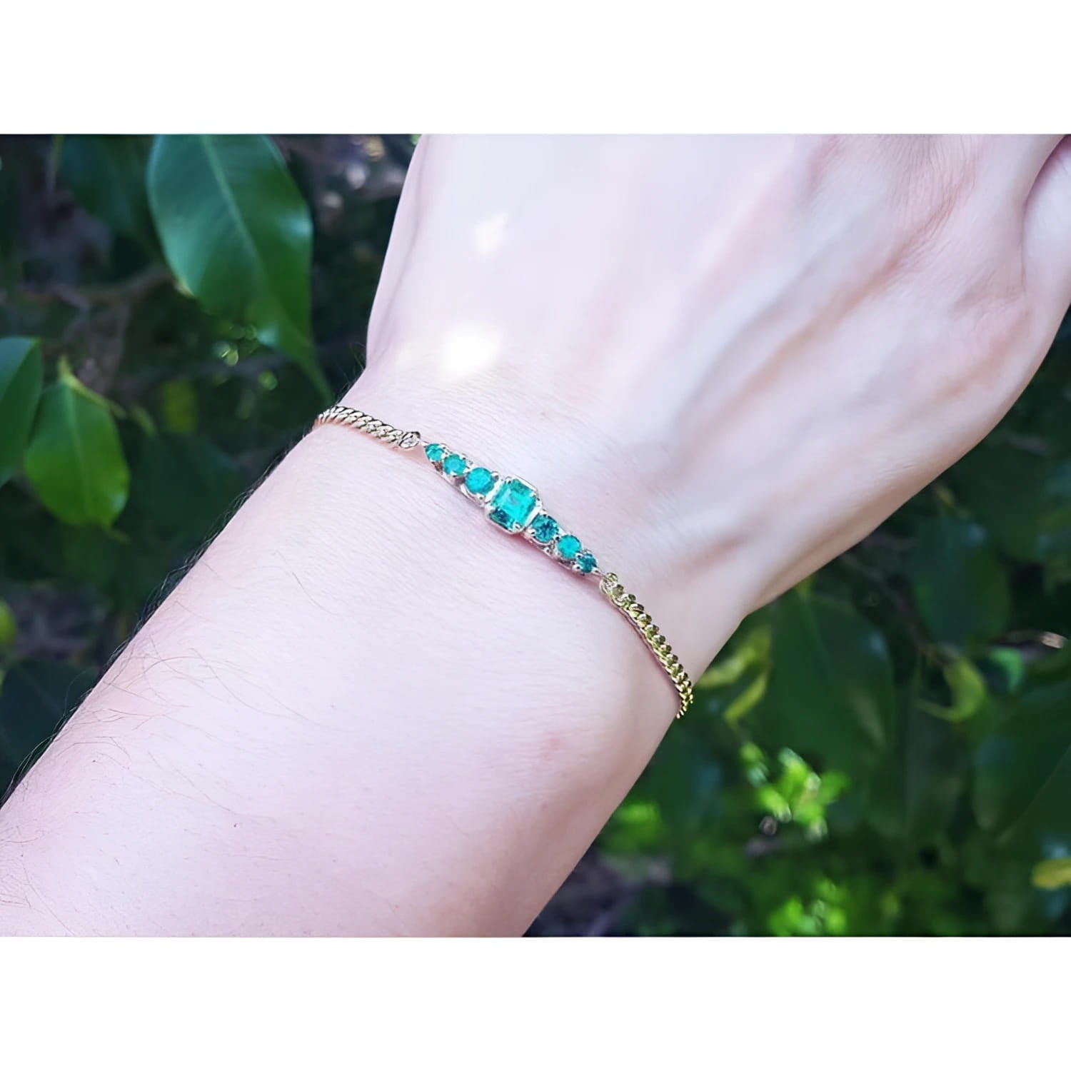 Women's 14K yellow gold bracelet with sparkling medium deep green Colombian emeralds on a wrist.