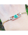 A 14k gold bracelet for women with a square natural emerald and diamonds displaying a vibrant medium-deep green color.