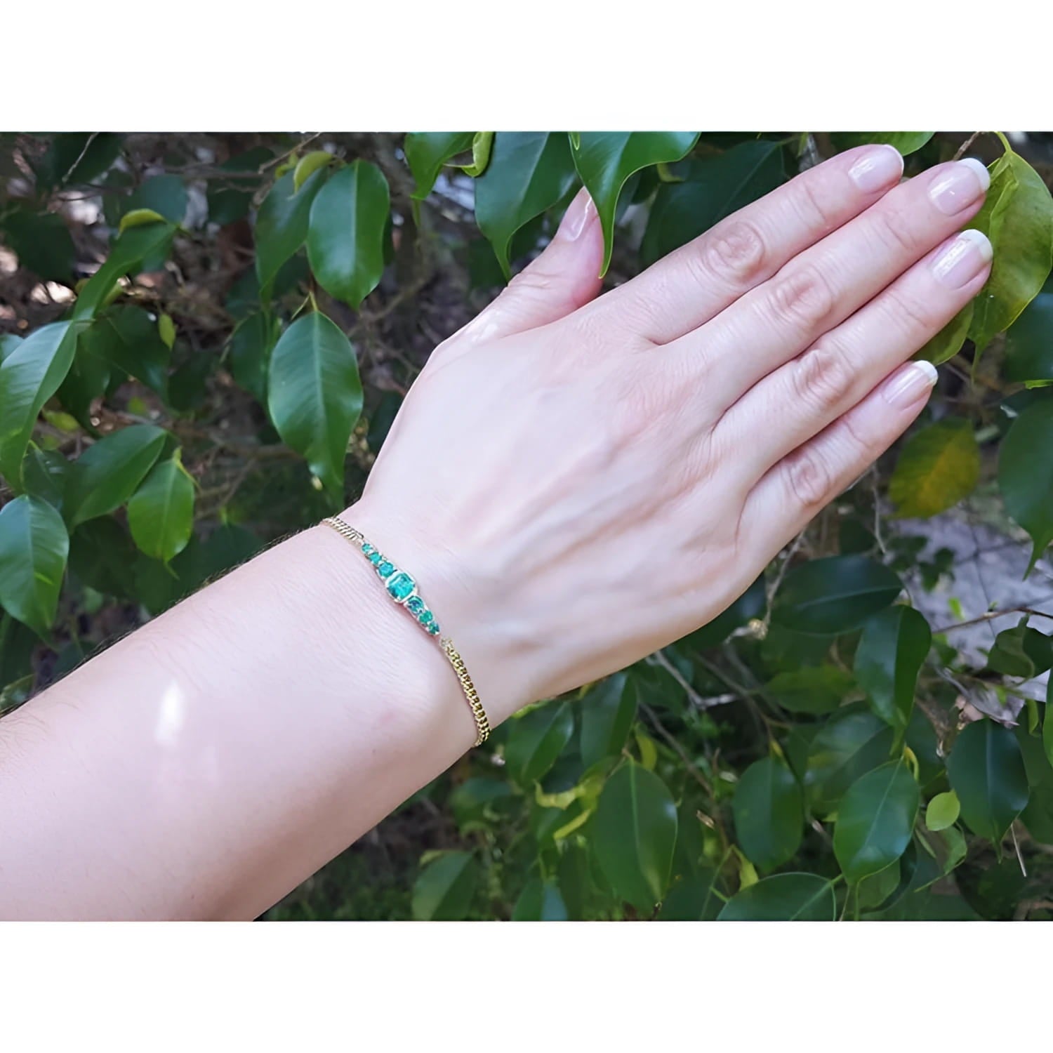 Women's 14K yellow gold bracelet with medium deep green Colombian emeralds on a wrist.