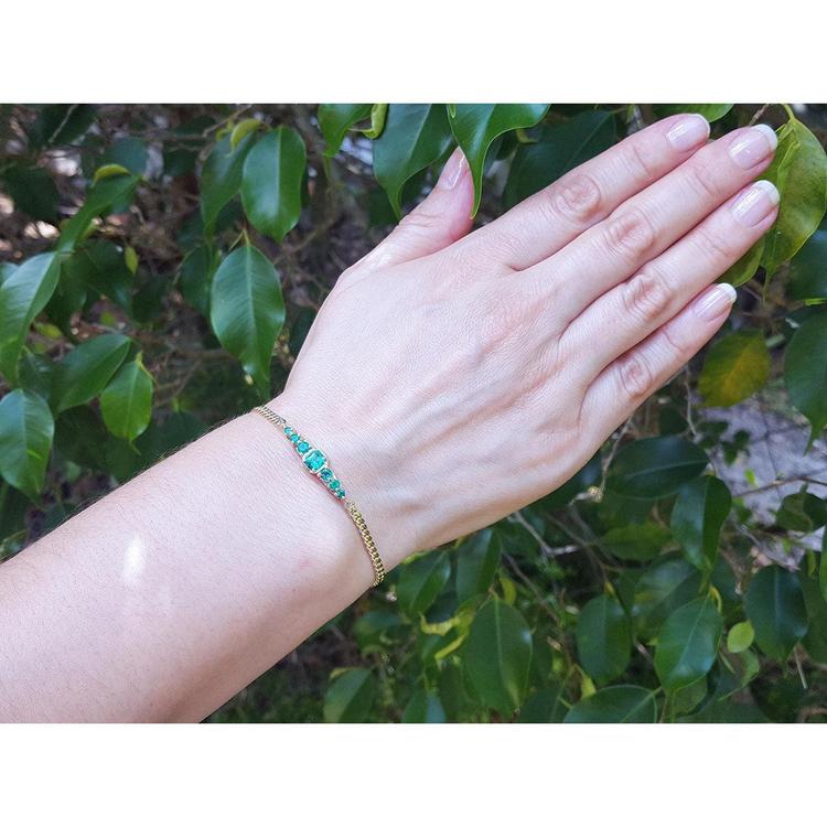 Women's 14K yellow gold bracelet with medium deep green Colombian emeralds on a wrist.