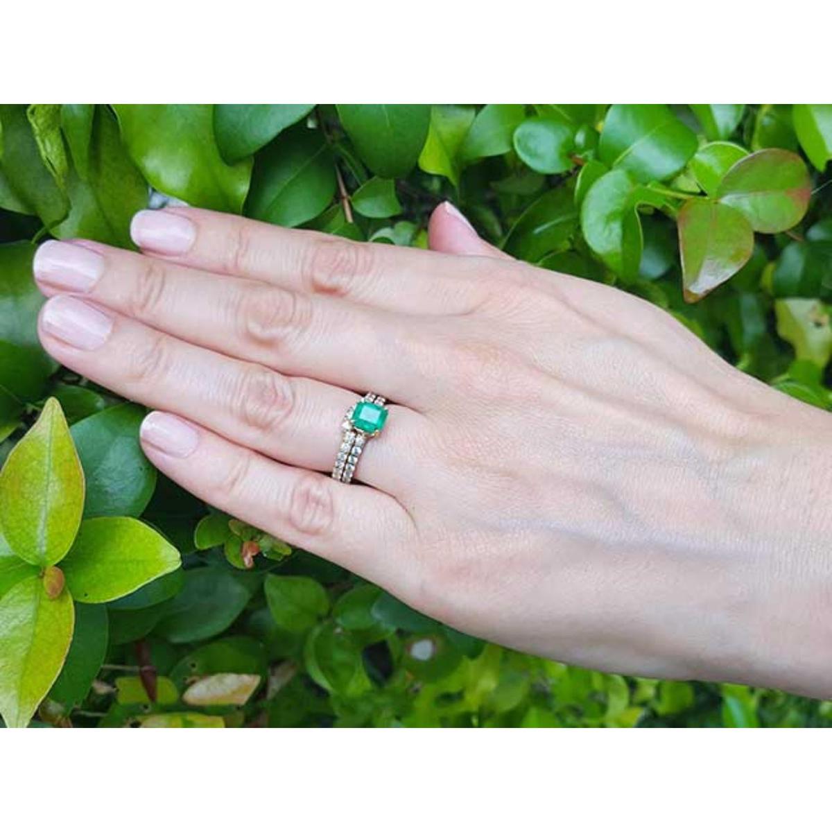 Hand wearing a ring with an emerald stone against a green leafy background