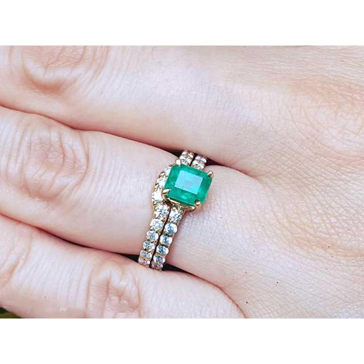 A colombian emerald bridal ring with matching band set in yellow gold on a finger.