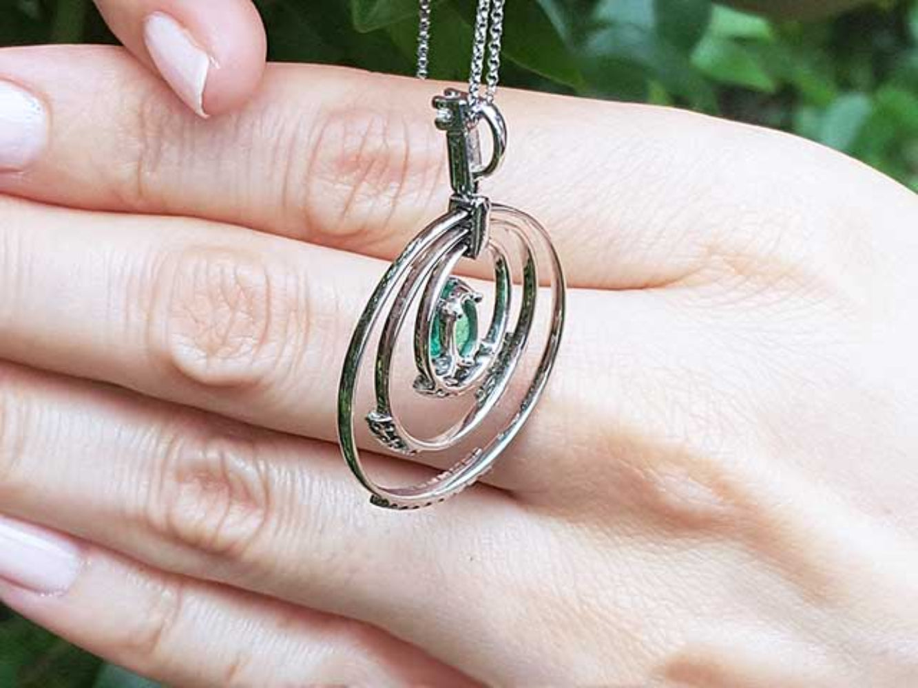 The back-side view of a circle of life emerald pendant held in a hand against a blurred natural background.