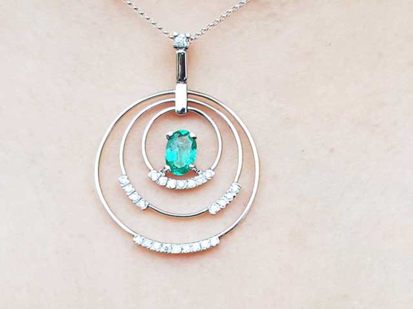 A triple circle of life pendant with an oval cut emerald on a light pink skin background.