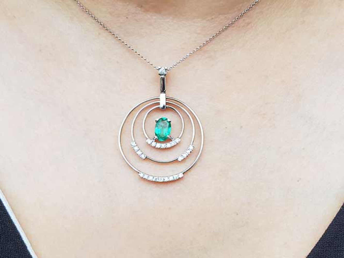 Necklace with a pendant featuring an emerald stone and small diamonds on a person&#39;s neck.