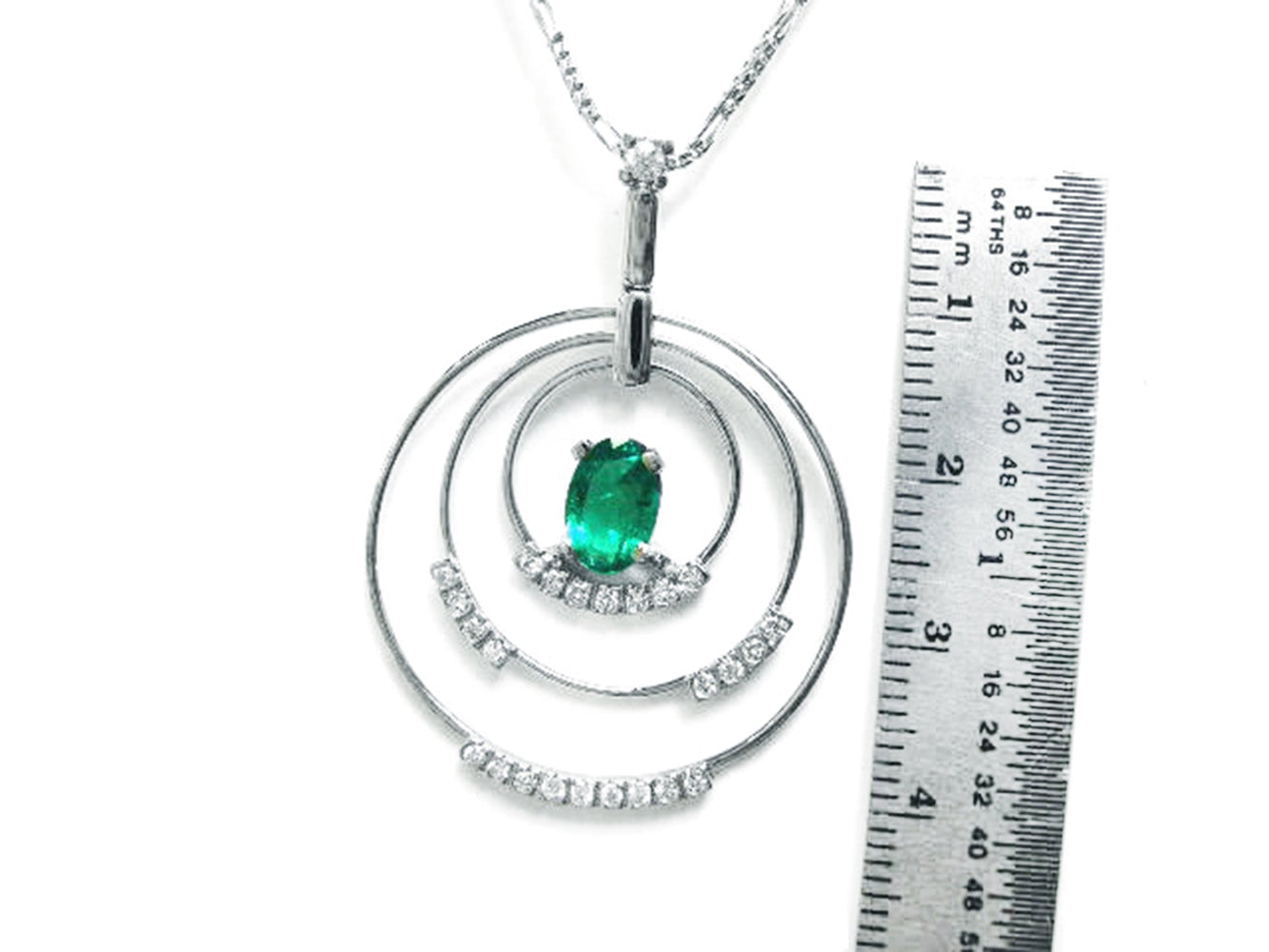 A triple circle of life natural emerald pendant next to a ruler for scale on a white background.