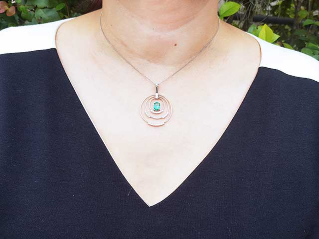 Necklace with three circles whit diamonds and in the enter an oval cut emerald worn by a woman against a natural background.