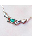 14K yellow gold Claddagh necklace with a heart-cut emerald held by two hands, worn on a neck.