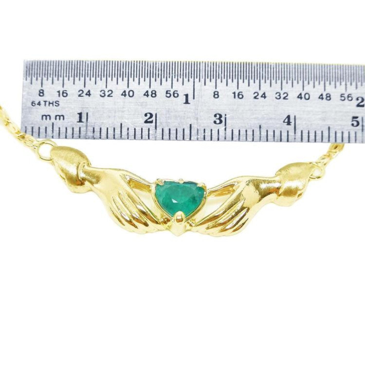 Emerald Claddagh necklace, heart-cut deep green emerald in 14K yellow gold, held by hands, with ruler for scale.