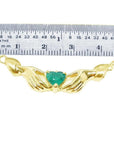 Emerald Claddagh necklace, heart-cut deep green emerald in 14K yellow gold, held by hands, with ruler for scale.
