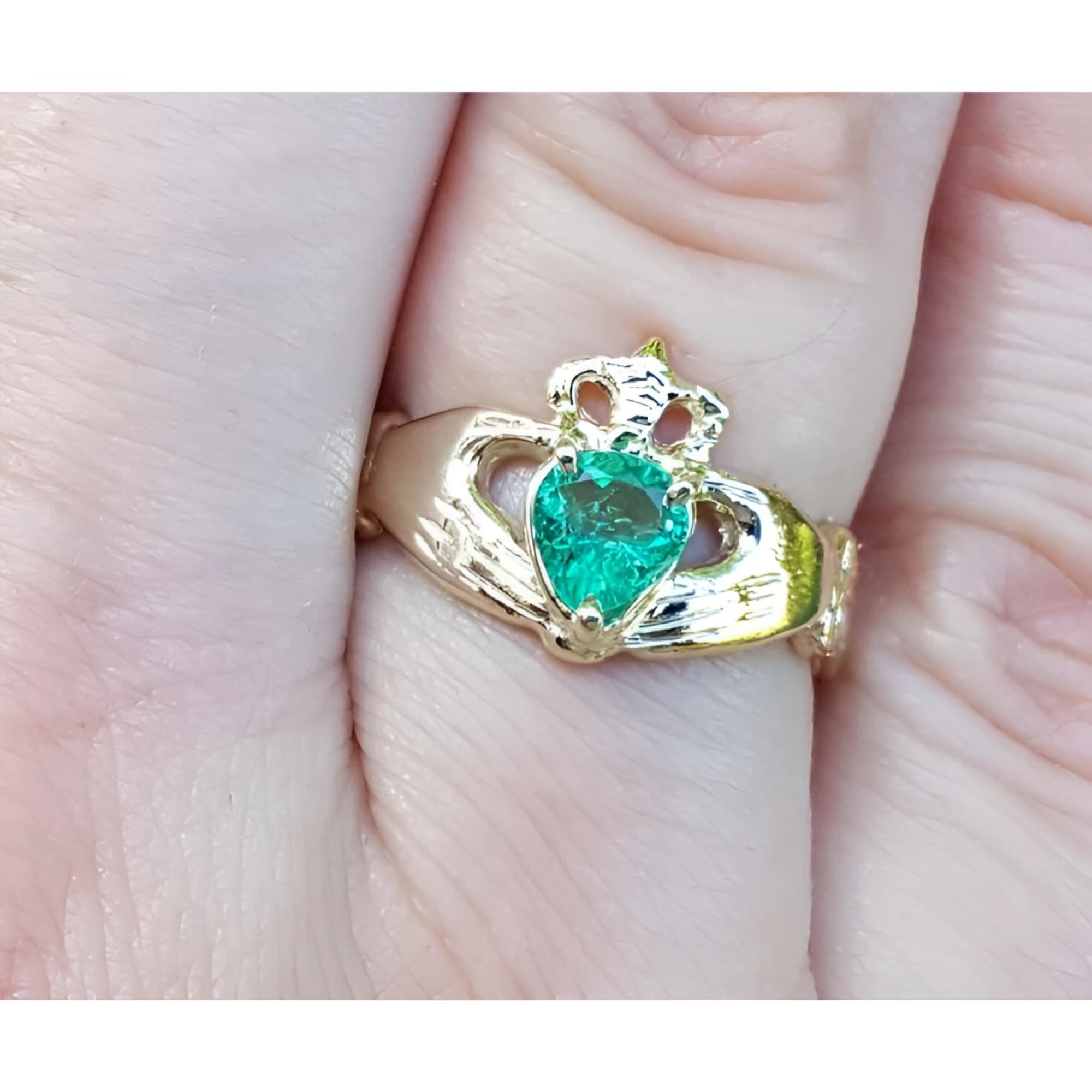 Emerald claddagh ring made of 14k yellow gold on a finger.