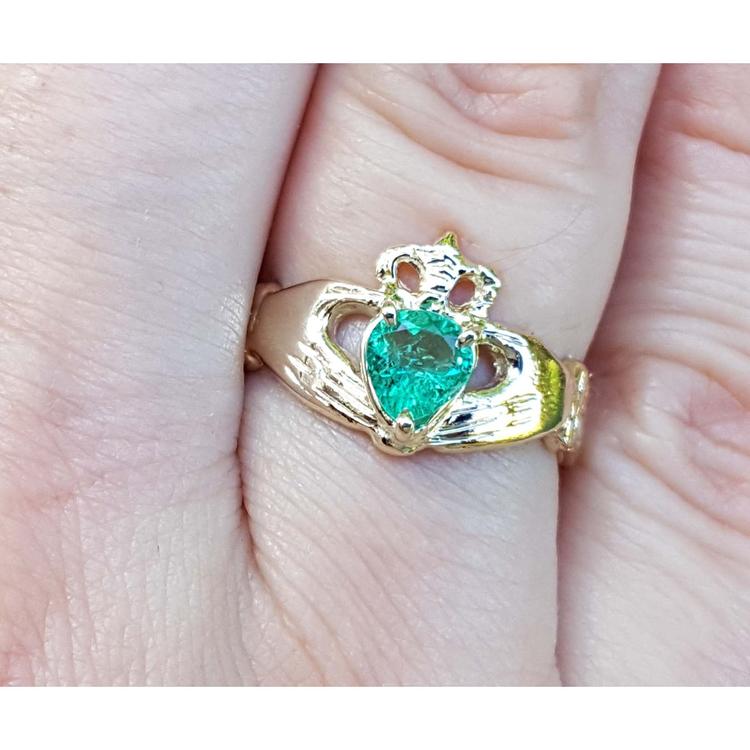 Emerald claddagh ring made of 14k yellow gold on a finger.