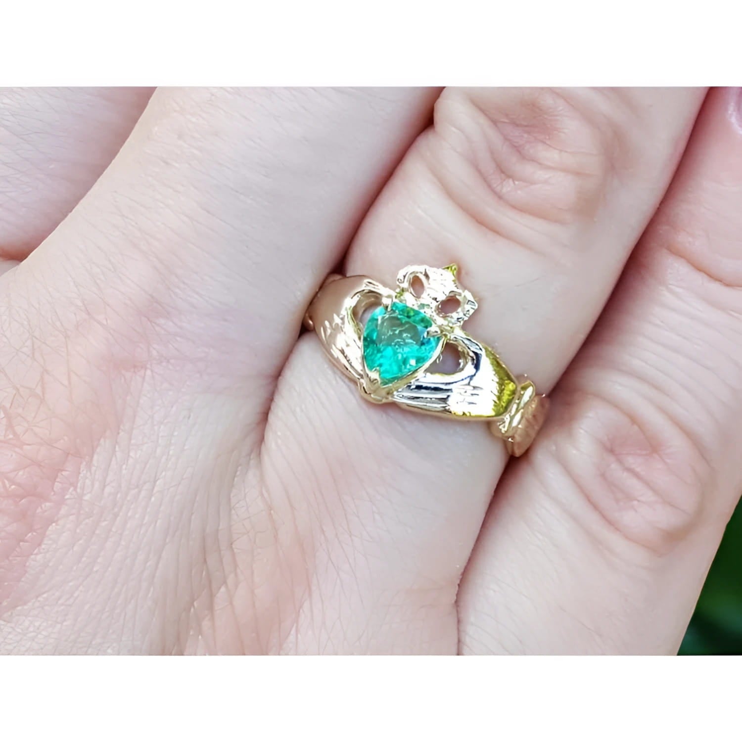 14K yellow gold Claddagh ring with a pear-shaped, medium-green emerald on a finger.