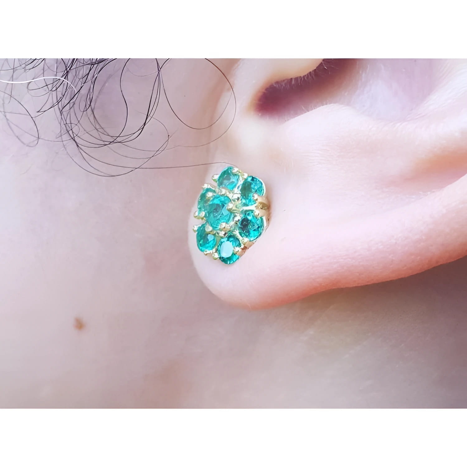 Colombian emerald cluster stud earring with six round-cut petals in 18K yellow gold on an ear.