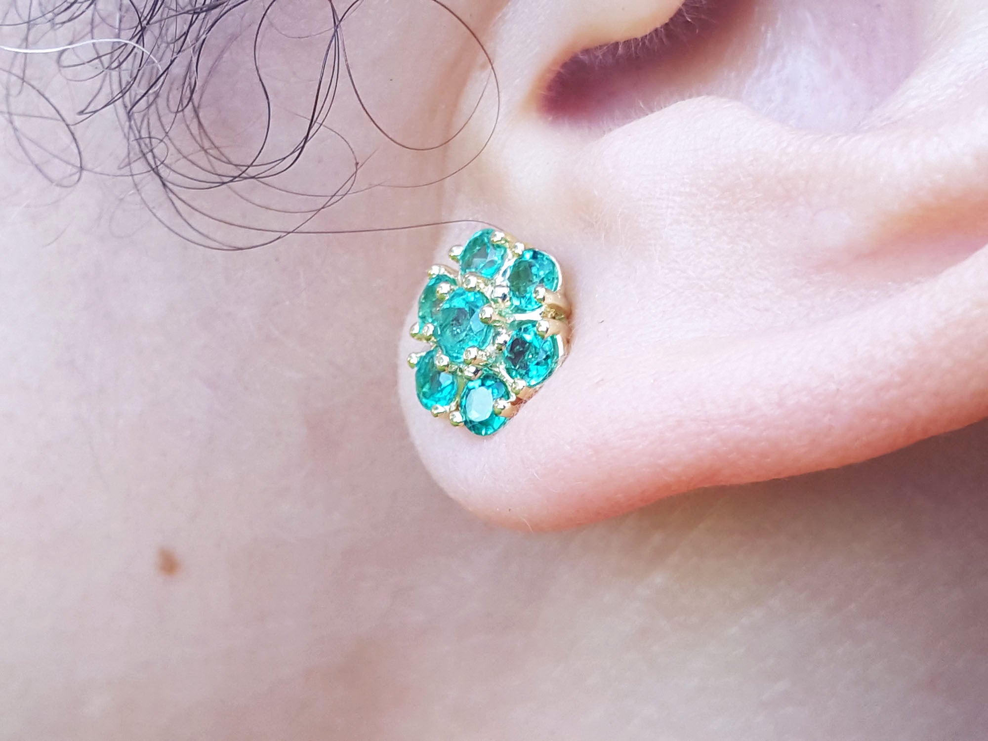 Close-up of an ear wearing a gold earring with natural emeralds.