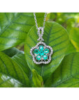14K white gold emerald cluster necklace with five petals, surrounded by diamonds, on a green leaf.