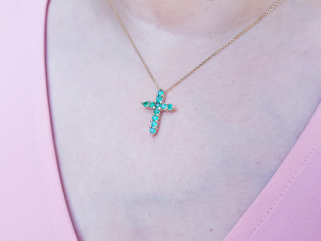 Necklace with a cross pendant featuring round natural emeralds worn on a person&#39;s neck.
